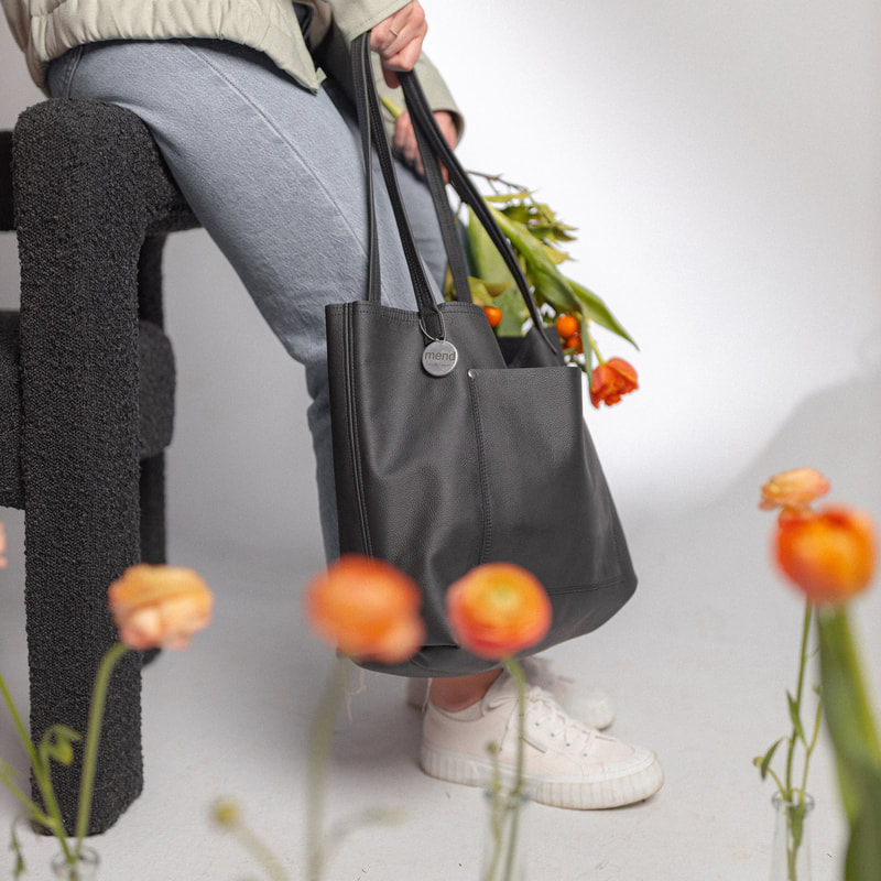 Lower half of woman wearing casual clothes and showcasing a large black purse with a floral arrangement bursting out.