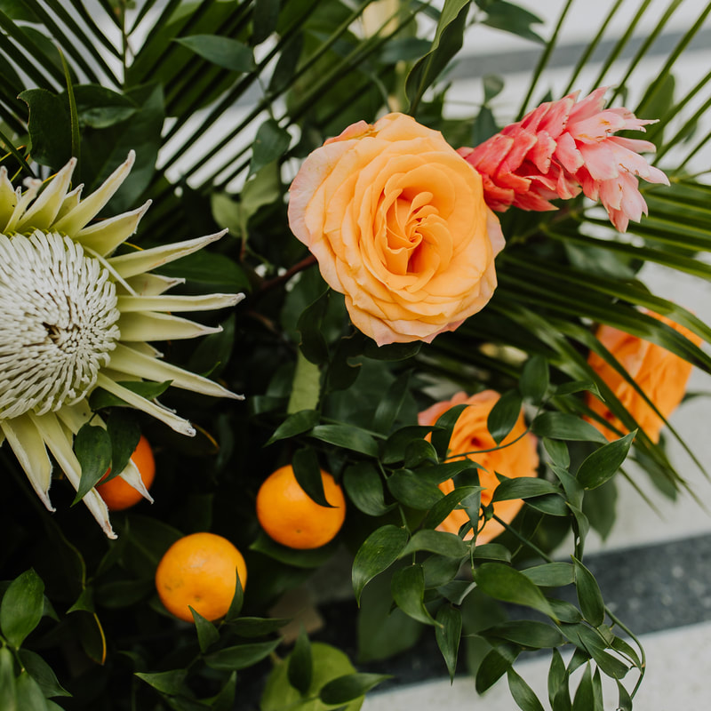 Tropical floral arrangement with bright pink and orange blooms amongst dark green foliage.